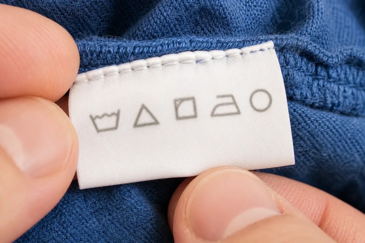 Étiquette textile avec symboles d&rsquo;entretien tenue entre deux doigts