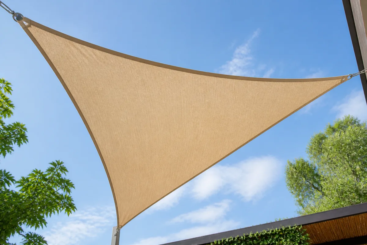 Voile d&rsquo;ombrage beige tendue au-dessus d&rsquo;une terrasse, coutures et œillets visibles